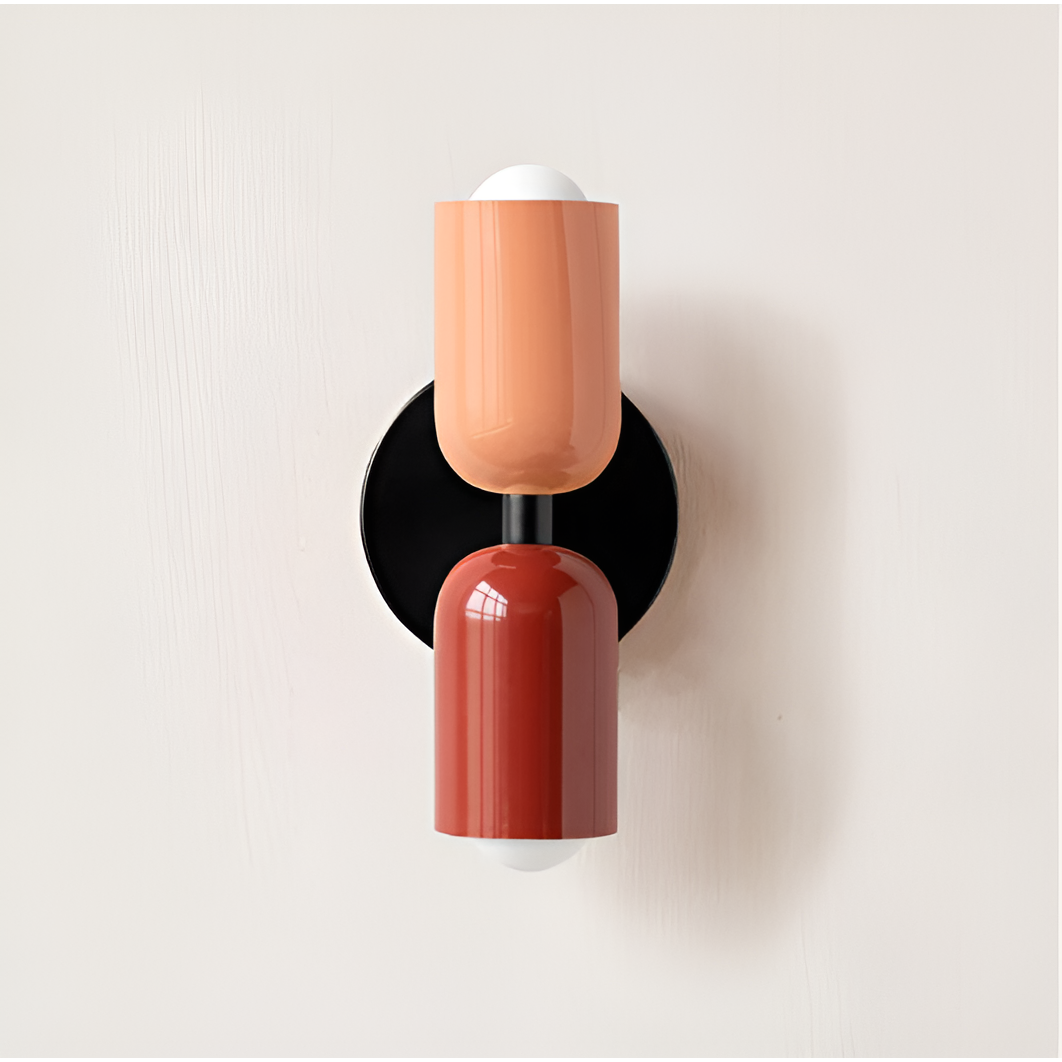 Close front view of a wall light with a peach upper head and red lower head on a black backplate. 18