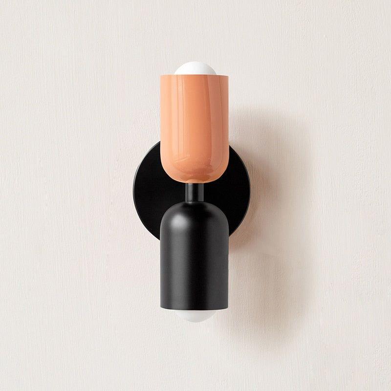 Wall light with a peach upper head and matt black lower head on a round black backplate, front view. 5