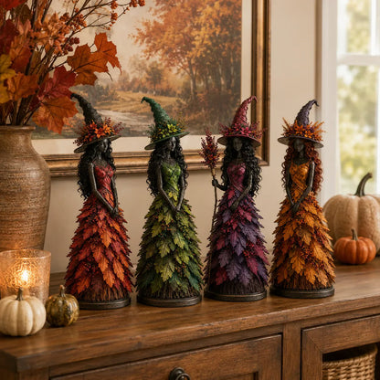 All four witch figurines in red, green, purple and golden-orange standing in a row on a wooden sideboard with pumpkins and a candle. 7