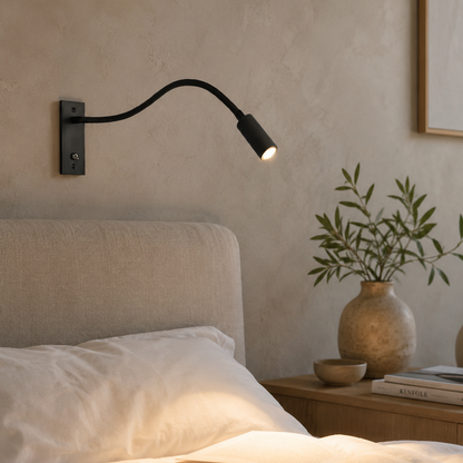 Black gooseneck reading light switched on above a bed with white linen, textured plaster wall and a vase of olive stems. 3