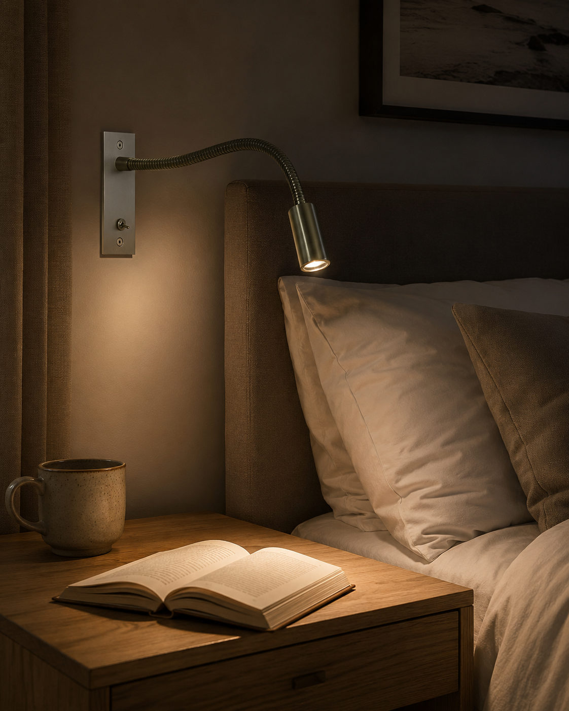 Brushed nickel reading light lit in a dim bedroom, shining over pillows and an open book on the bedside table. 8