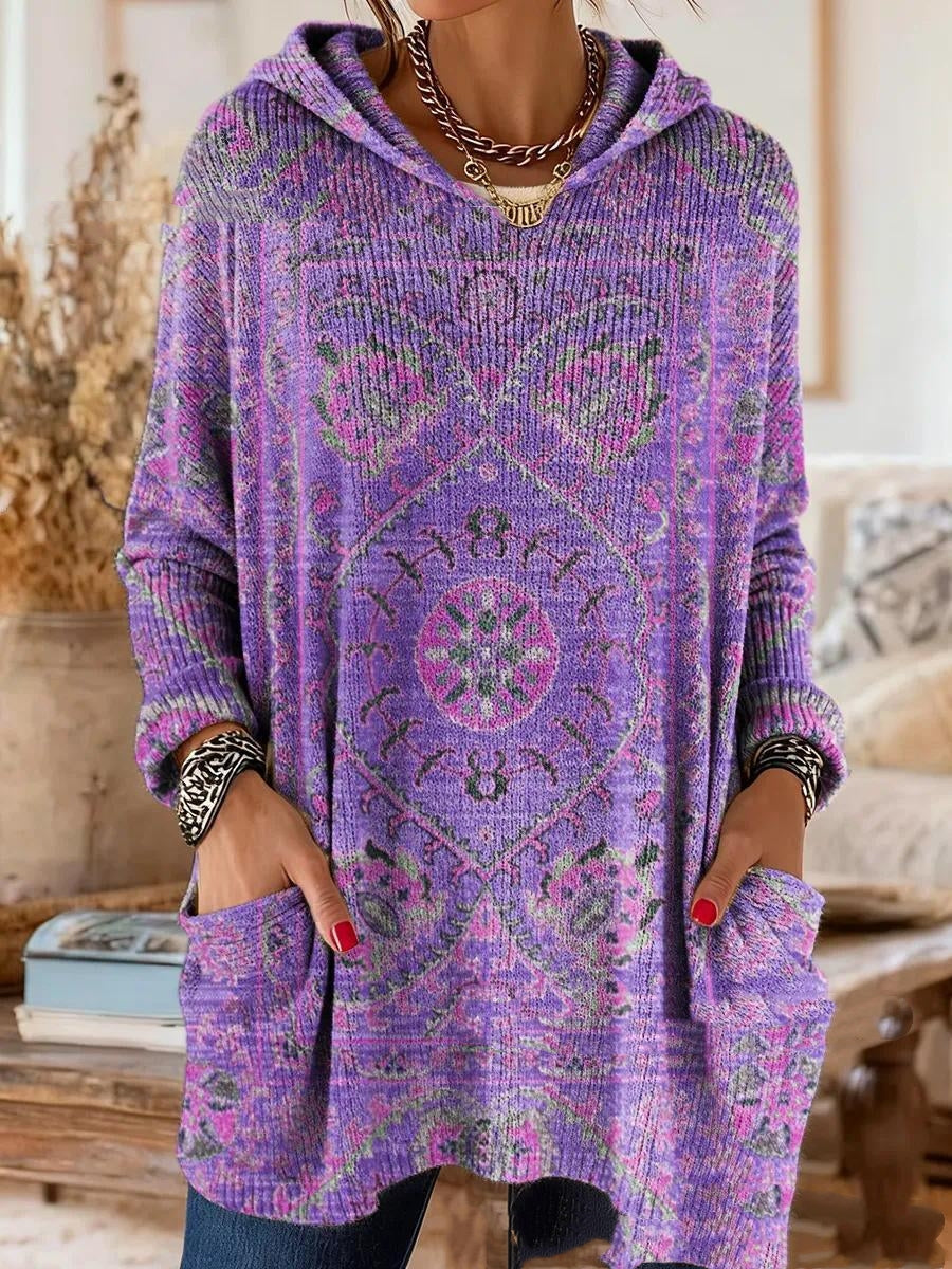 Hooded tunic in purple with a pink and green medallion print, worn by a model with hands in the front pockets. 2