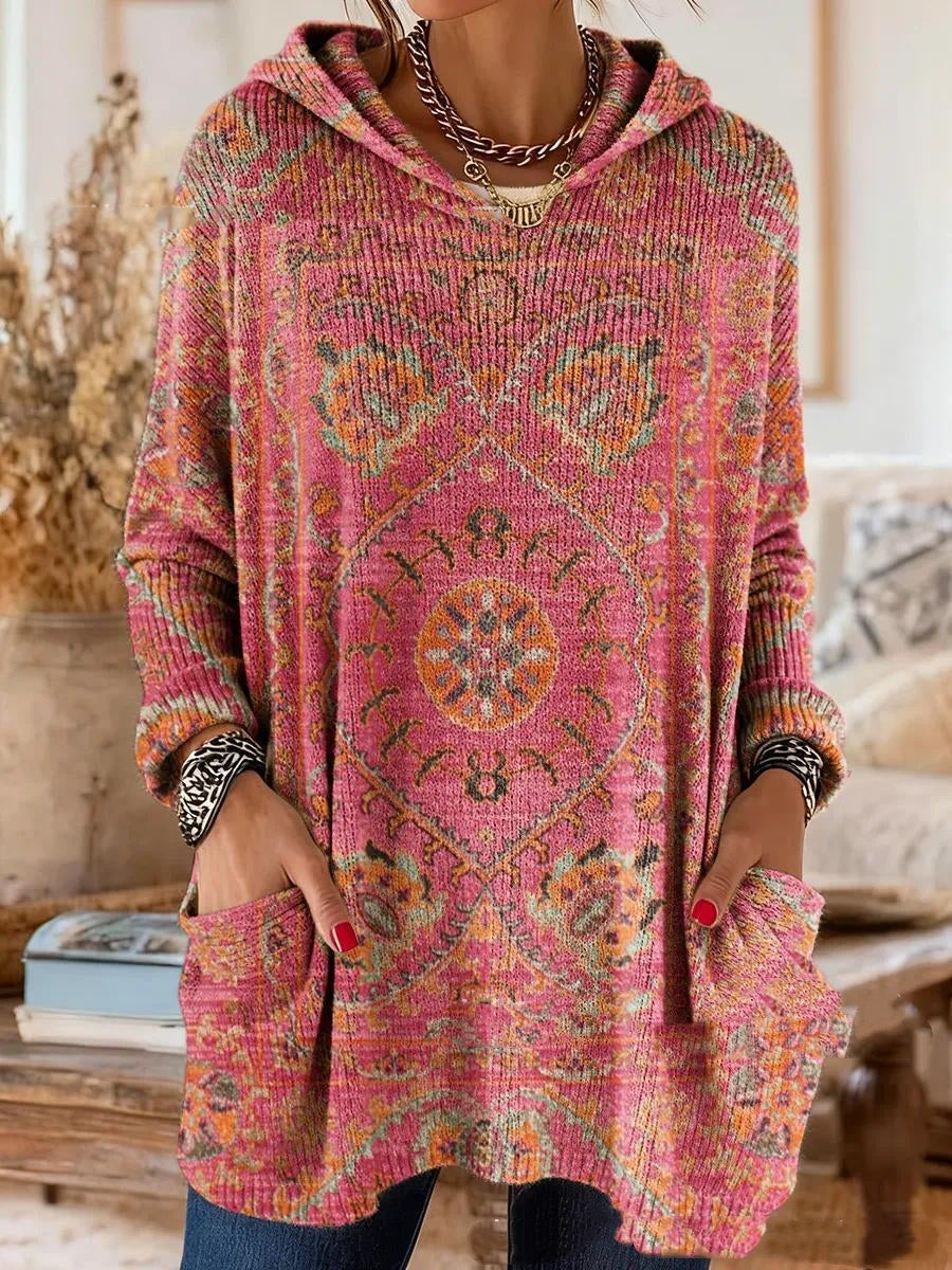 Hooded tunic in pink with an orange and green medallion print, worn by a model with hands in the front pockets. 6