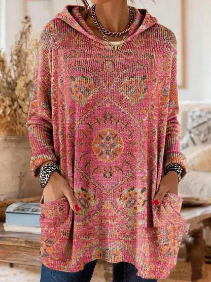 Hooded tunic in pink with an orange and green medallion print, worn by a model with hands in the front pockets. 6