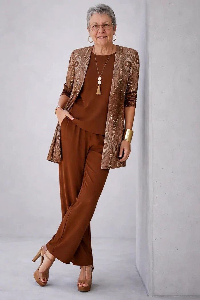 Older model in rust brown top and trousers with a patterned sequin-look cardigan, leaning on a wall 9