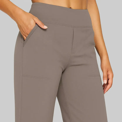 Close-up of the taupe trousers' wide waistband, front pocket opening and stitched patch pocket, with a hand in the pocket. 3