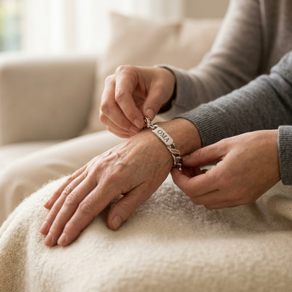 Close view of one person fastening the silver chain bracelet on an older woman's wrist, resting on a cream blanket. 3