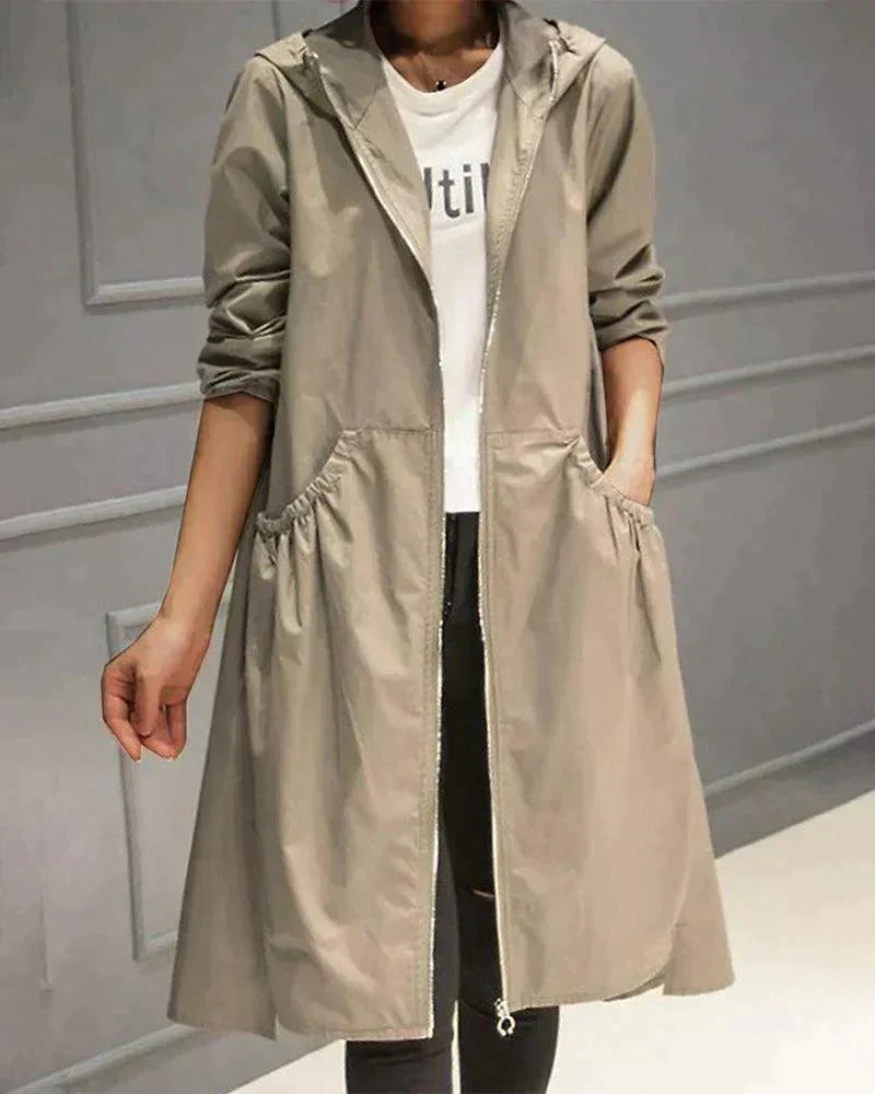 Model wearing the hooded raincoat in light khaki, open over a white top, one hand in a gathered pocket 1