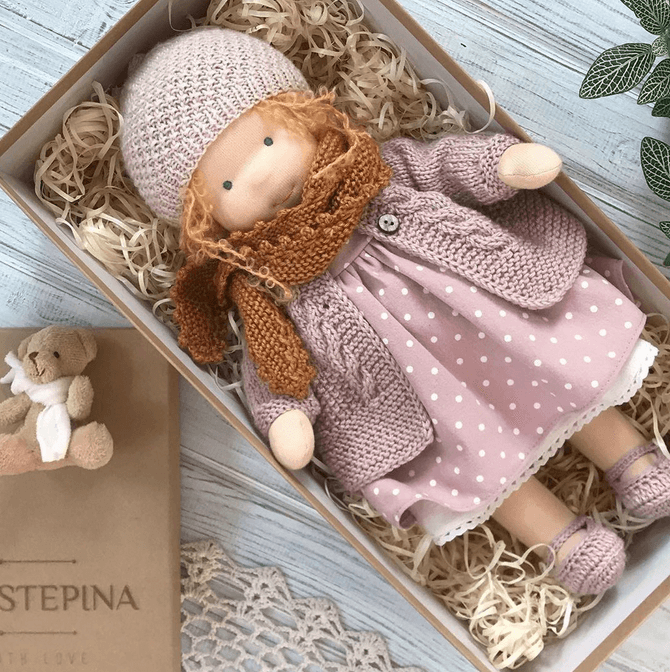Doll in a mauve knitted hat and cardigan, spotted pink dress and rust scarf, lying in a gift box 5
