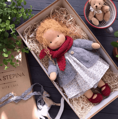 Ginger-haired doll in red scarf, grey cardigan, patterned dress and red shoes, boxed with a teddy in a cup nearby 9