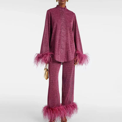 Model wearing the set in berry pink glitter, with a high collar, buttoned shirt and wide trousers, holding a small gold bag. 1