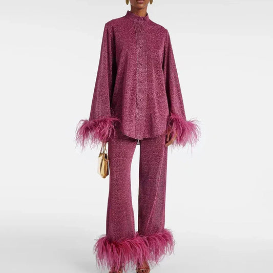 Model wearing the set in berry pink glitter, with a high collar, buttoned shirt and wide trousers, holding a small gold bag. 1