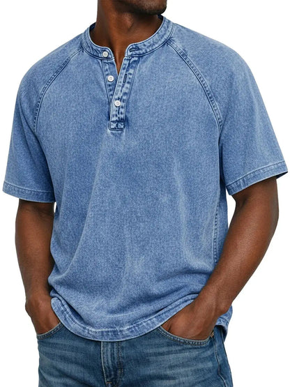 Model wearing the short-sleeved raglan Henley in a washed light blue, with a three-button placket, worn with blue jeans. 2