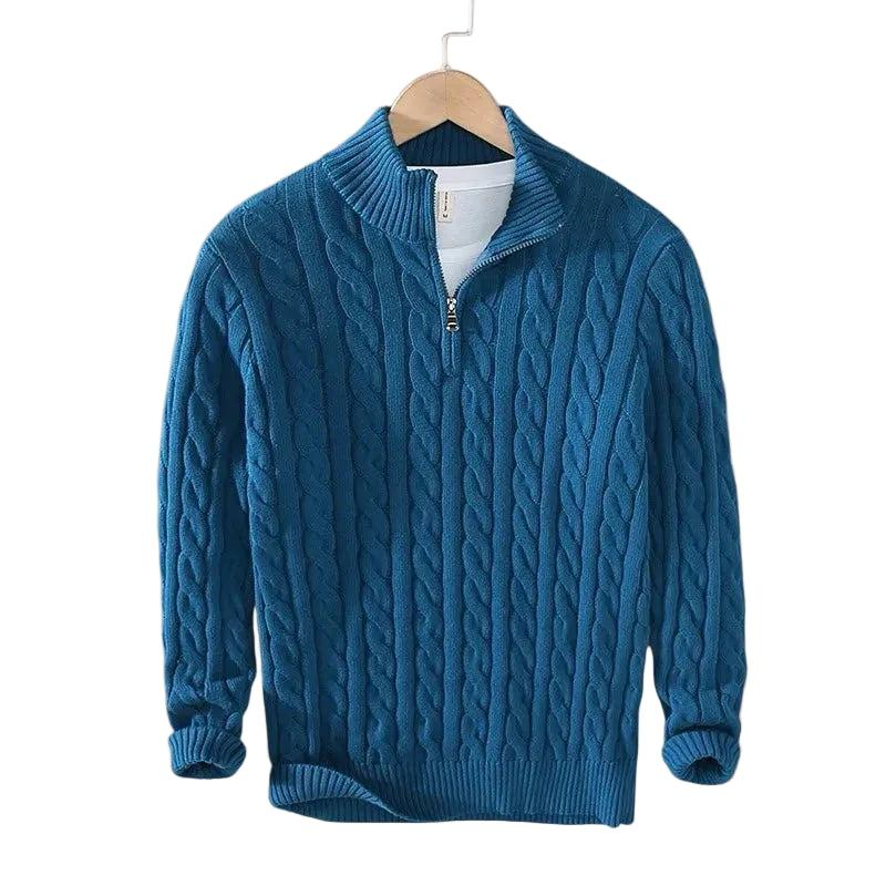 Deep teal blue cable knit jumper with ribbed mock neck and short zip, displayed on a wooden hanger over a white top. 5