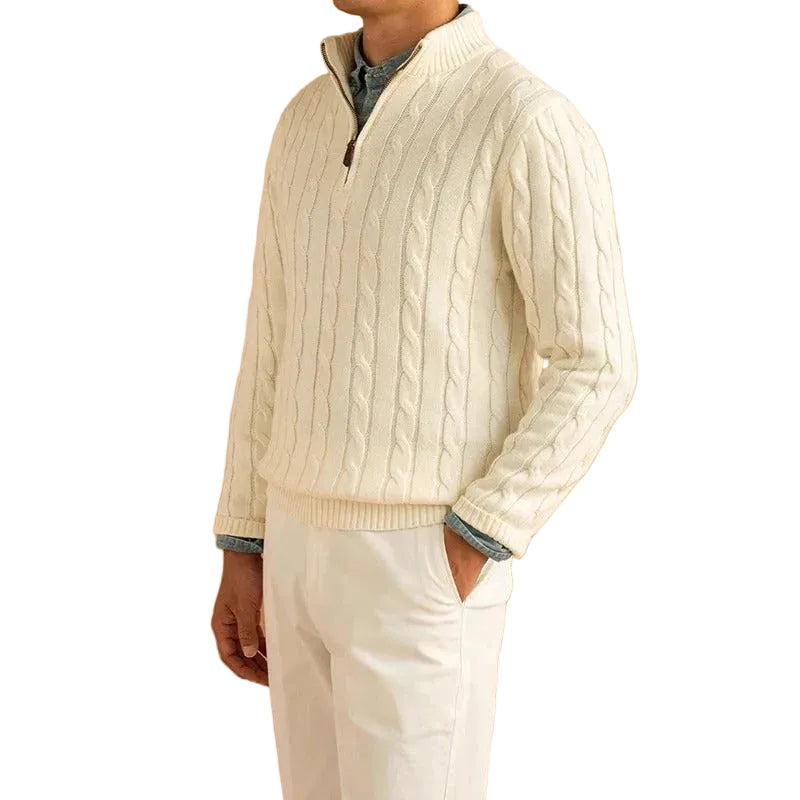 Man wearing the cream cable knit jumper with a partly unzipped mock neck, over a blue shirt and cream trousers, hand in pocket. 1