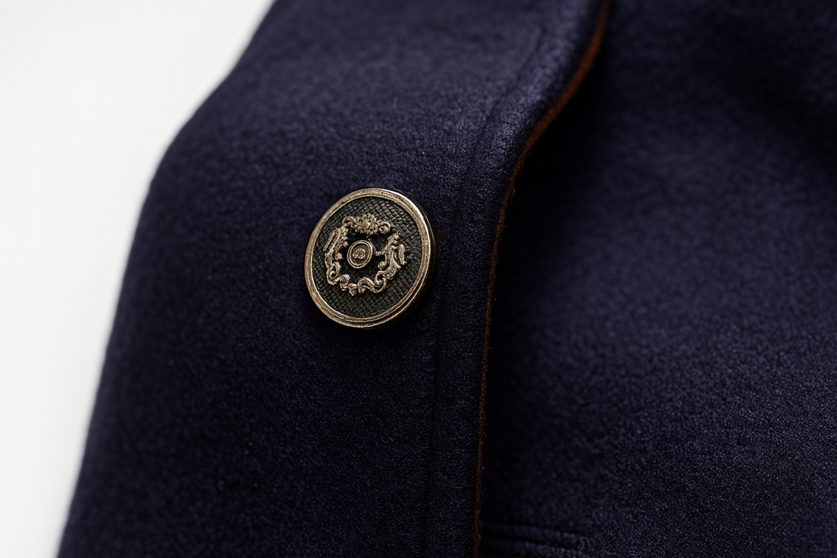 Close-up of a navy coat front with an ornate metal button and fine tan edging 10