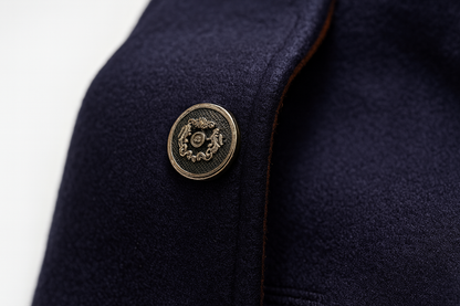 Close-up of a navy coat front with an ornate metal button and fine tan edging 10