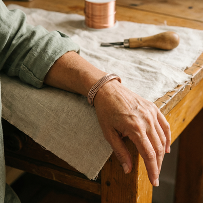 Copper cuff with a rope-style pattern worn on a wrist resting on a workbench 2