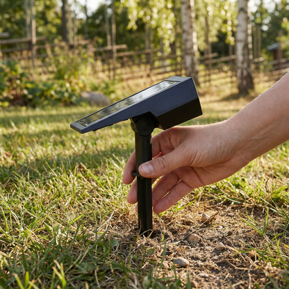 Hand pushing the spotlight's ground stake into grass, showing the tilting solar panel head in daylight 4