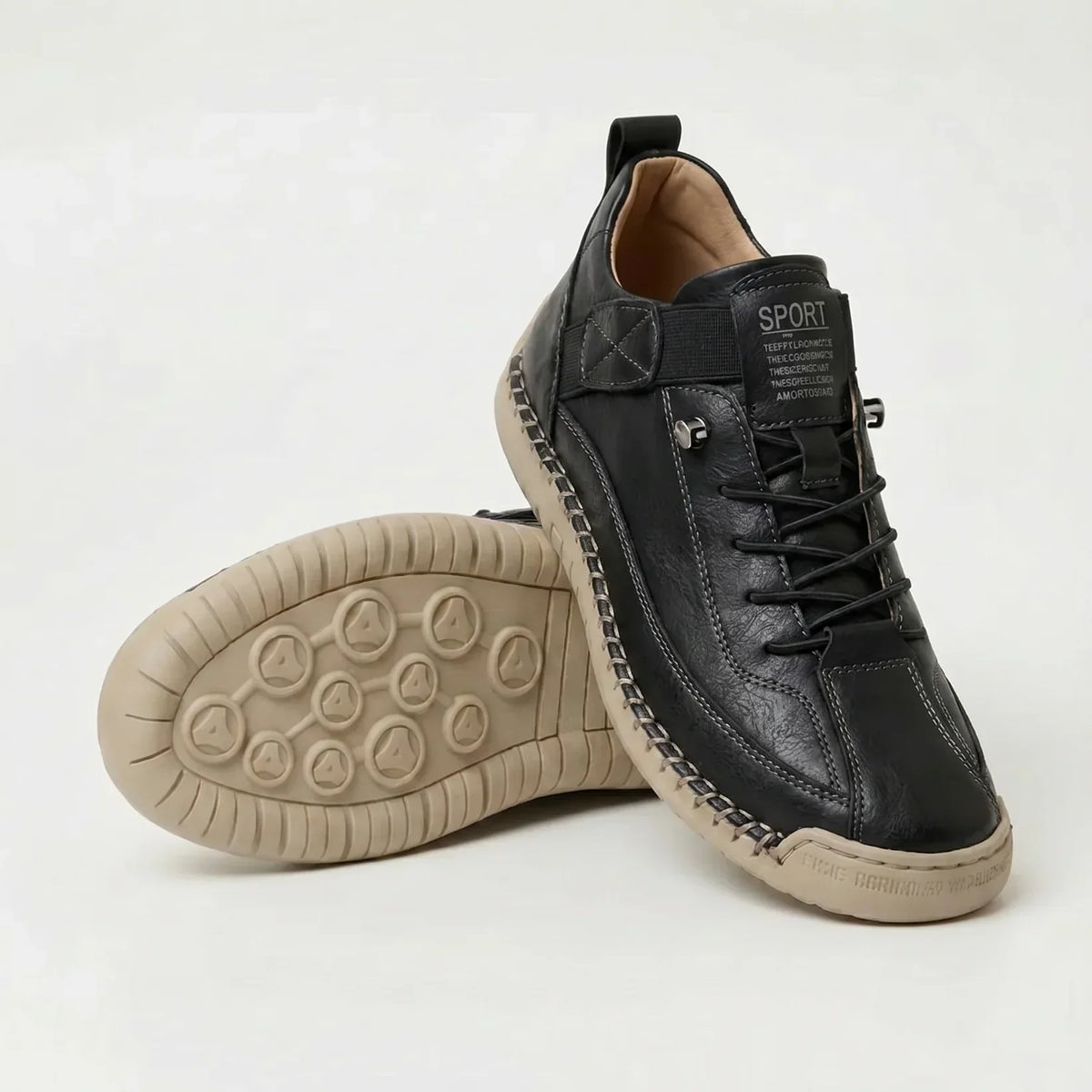 Black trainers with grey stitching and a beige sole, one shoe angled upright and one showing the studded tread pattern. 12