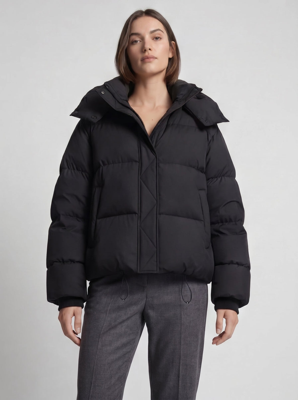 Close-up of a model wearing the black puffer jacket with hood up, paired with grey trousers 6