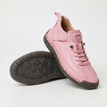 Pink lace-up trainers with a dark grey sole and orange stitching, one shoe upright and one tilted to show the studded outsole. 14