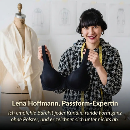 Smiling fit expert in a tweed jacket holding up the black bra in a design studio, next to a dress form. 5