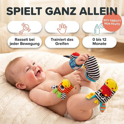 Smiling baby lying on a knitted blanket wearing the animal-faced wrist rattles and striped foot rattle socks, gripping one sock. 1