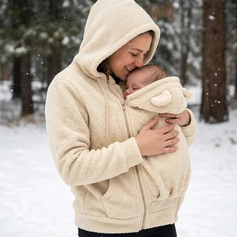 Woman in a cream sherpa hoodie kissing her baby's head in falling snow, baby wrapped in the eared carrier panel. 8