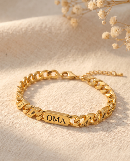 Gold curb chain bracelet with engraved central bar and name links lying on creamy linen beside dried flowers. 4