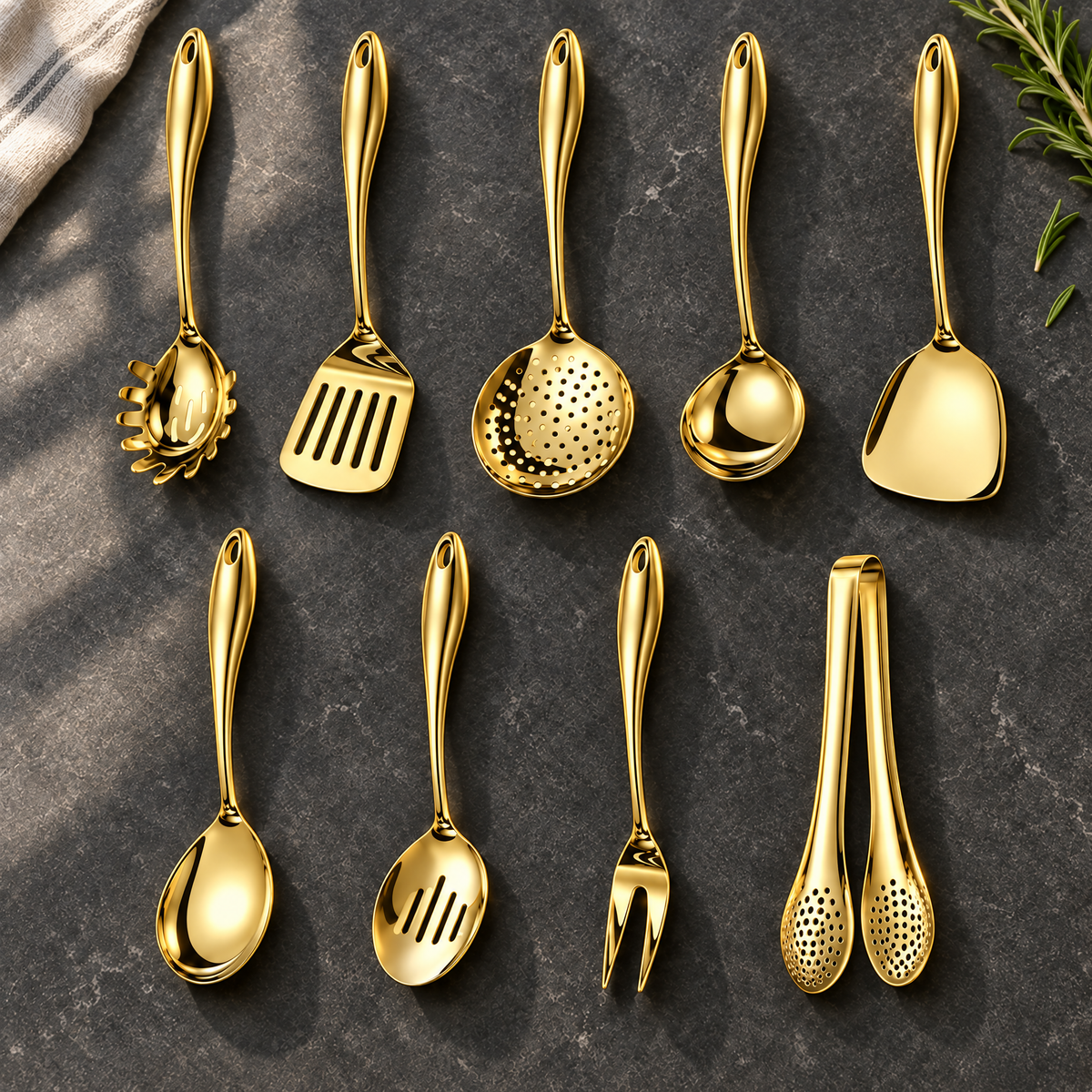 Nine gold-coloured utensils in two rows on dark stone with a cloth and rosemary, including skimmer, wok turner, ladle, fork and tongs. 25