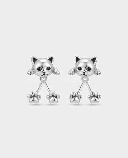 Pair of silver-tone cat head earrings with black eyes and two dangling paw prints each, on plain white 1