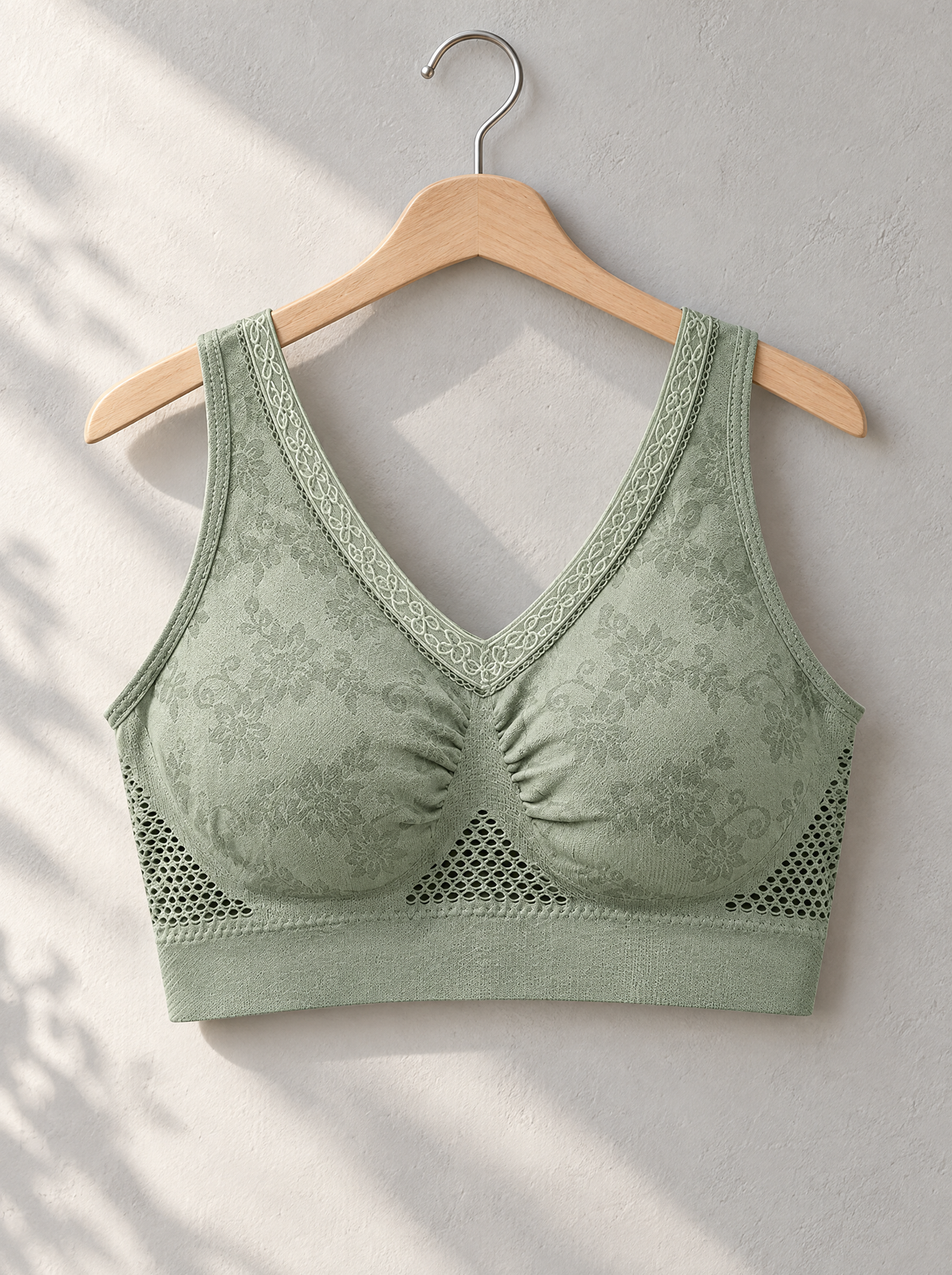 Green bra hanging on a wooden hanger against a light wall, with sunlight and shadows falling across it 4