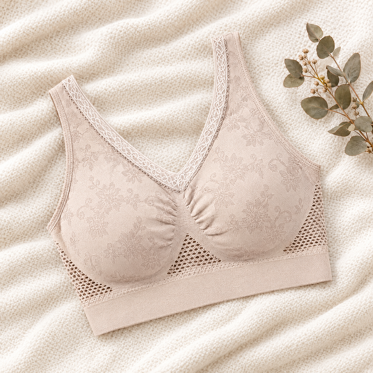Beige bra laid flat on a cream knit blanket beside a eucalyptus sprig, showing floral jacquard and lace trim 1