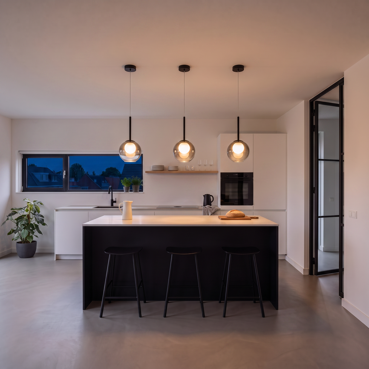 Smoke grey globe pendants glowing warmly over a kitchen island at dusk, with the window dark blue 5