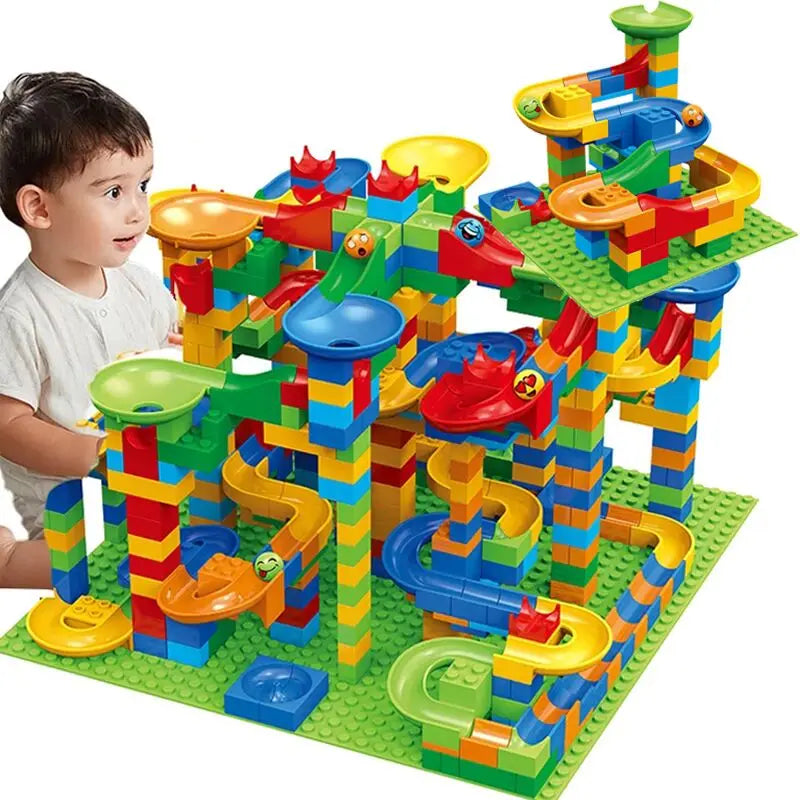 Young child in a white top looks at a tall, elaborate marble run with funnels, slides and a second raised baseplate. 6