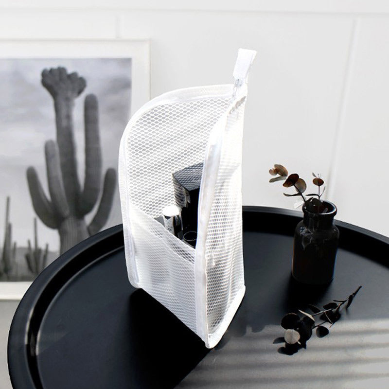 White mesh pouch standing upright on a round black side table, with toiletries visible through the open front pocket and a cactus print behind. 2