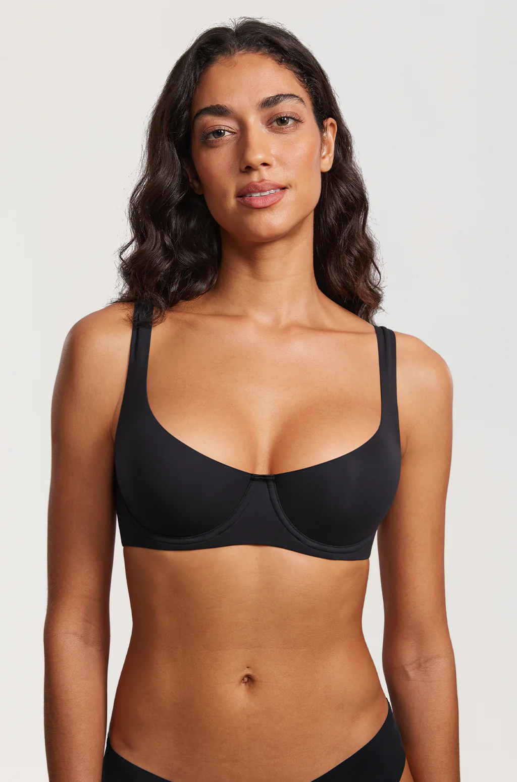 Front view of a model standing in the black balconette bra and black briefs against a plain light background. 12