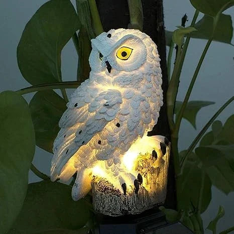 Close-up of a white owl light glowing warmly on its stump perch among large green leaves. 8