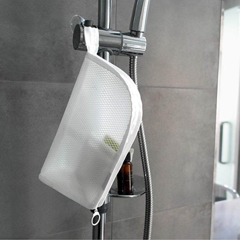 White mesh pouch hanging by its loop from a shower rail in a grey-tiled bathroom, with a bottle on the shelf below. 4