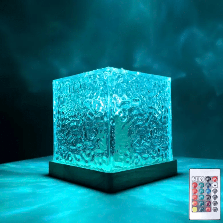 Rippled glass cube lamp with a wooden base glowing turquoise in a dark room, with its small remote control beside it. 1