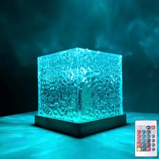Rippled glass cube lamp with a wooden base glowing turquoise in a dark room, with its small remote control beside it. 1