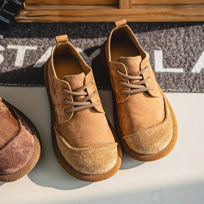 Tan lace-up shoes seen from above and slightly to the side, resting on a grey doormat beside a pair in a darker shade. 2
