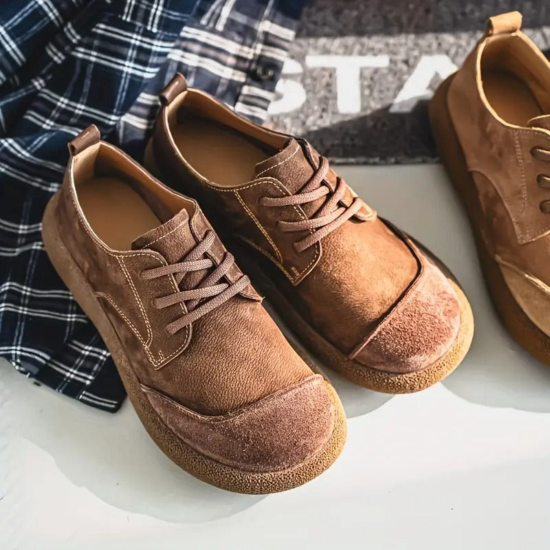 Brown and tan lace-up shoes with suede toe caps and contrast stitching, arranged beside a blue and white checked shirt. 11