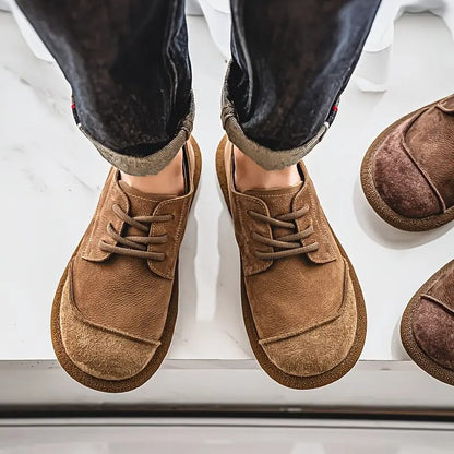 Top-down view of a man wearing tan lace-up shoes with rolled dark jeans, with brown pairs just visible at the edge. 4