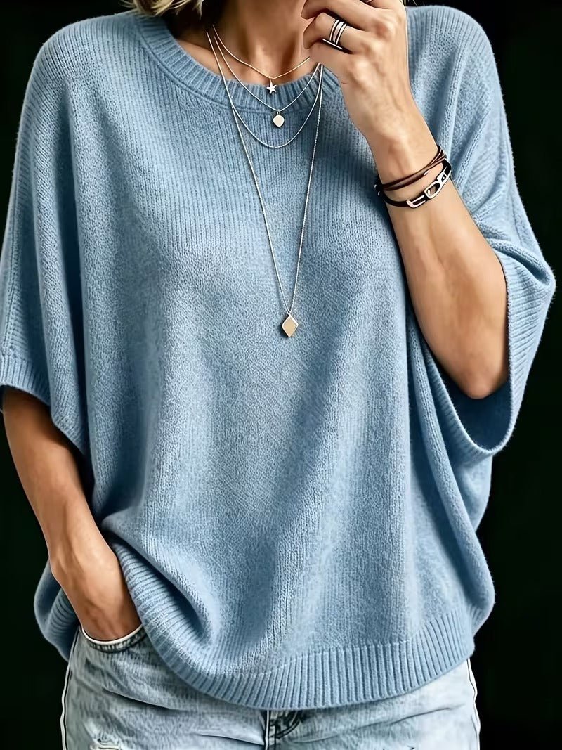 Close-up front view of the light blue batwing knit top with a hand in a jeans pocket and layered necklaces. 12