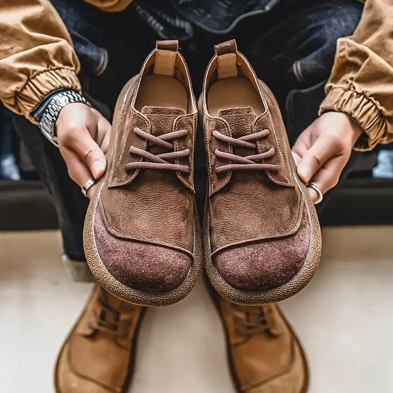 Hands holding a pair of brown suede lace-up shoes close to the camera, with tan pairs of shoes underneath. 10