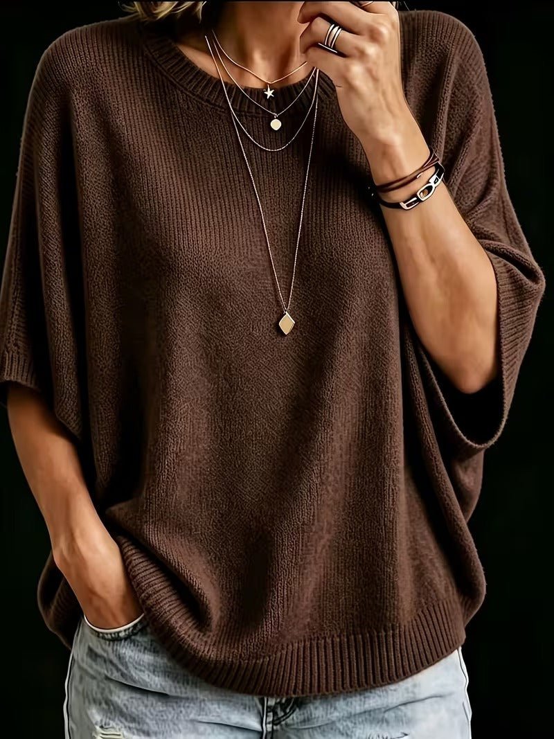Close-up front view of the dark brown batwing knit top worn with layered necklaces and a hand in a jeans pocket. 17