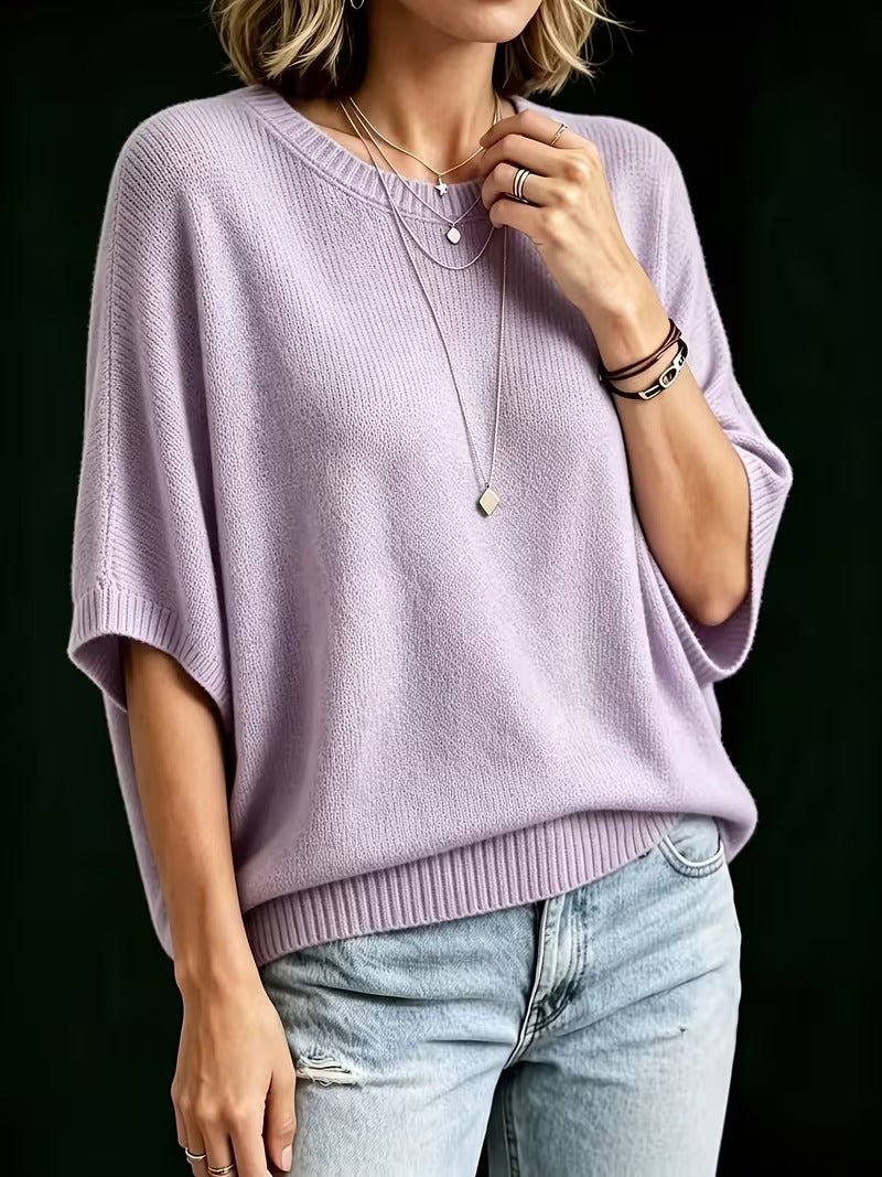 Three-quarter view of a model in the lilac knit top with one hand at the collarbone, showing the batwing sleeves. 8