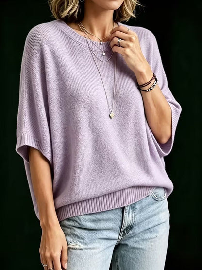 Three-quarter view of a model in the lilac knit top with one hand at the collarbone, showing the batwing sleeves. 8